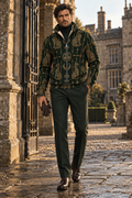 A man wearing a dark green and gold patterned zip-up jacket, dark green trousers, and brown leather shoes walks along a stone courtyard path next to a large stone building.