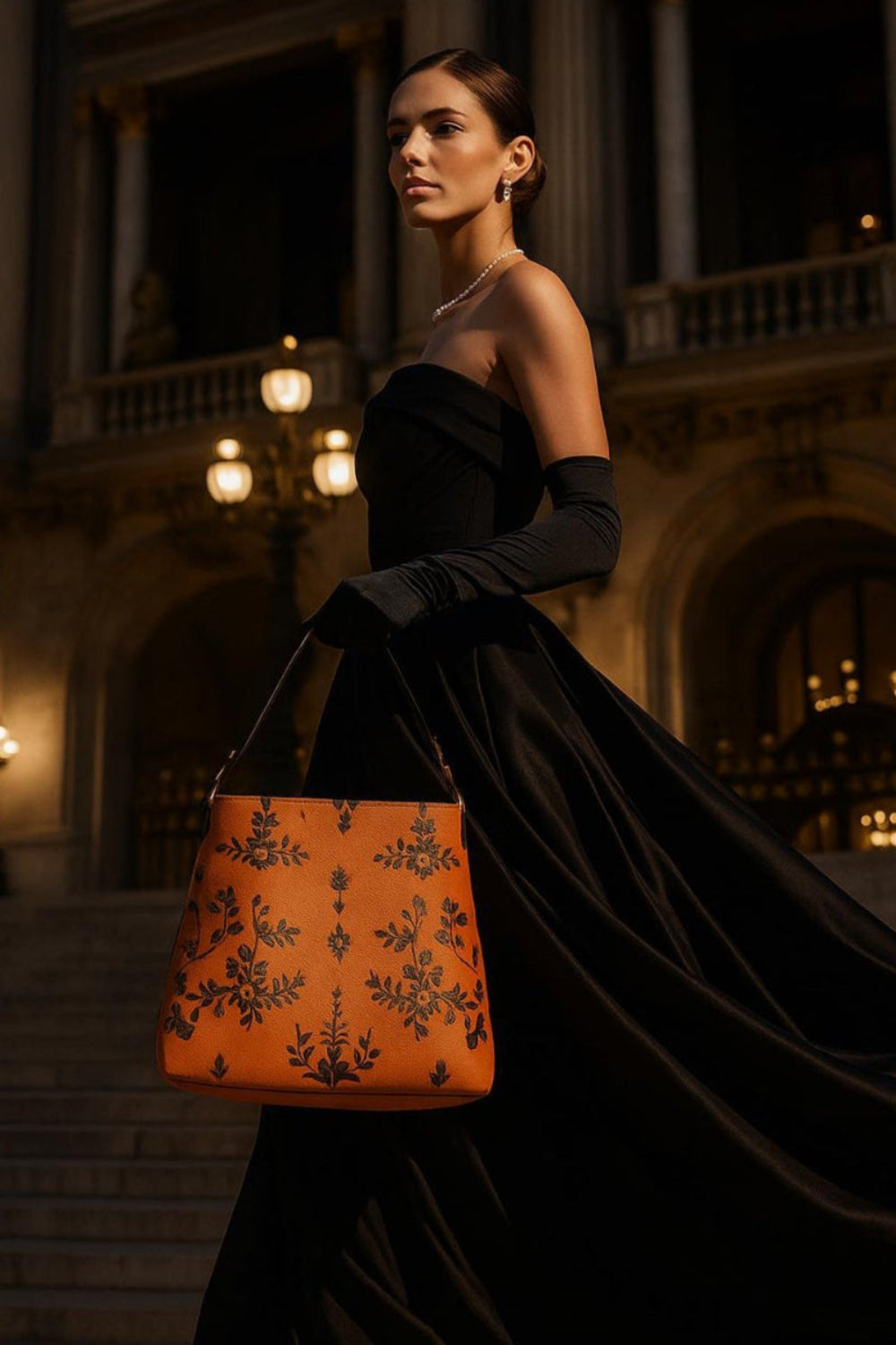 Elegant woman in black gown holding orange baroque bucket bag from Angelic Blessings Shop outdoors at night