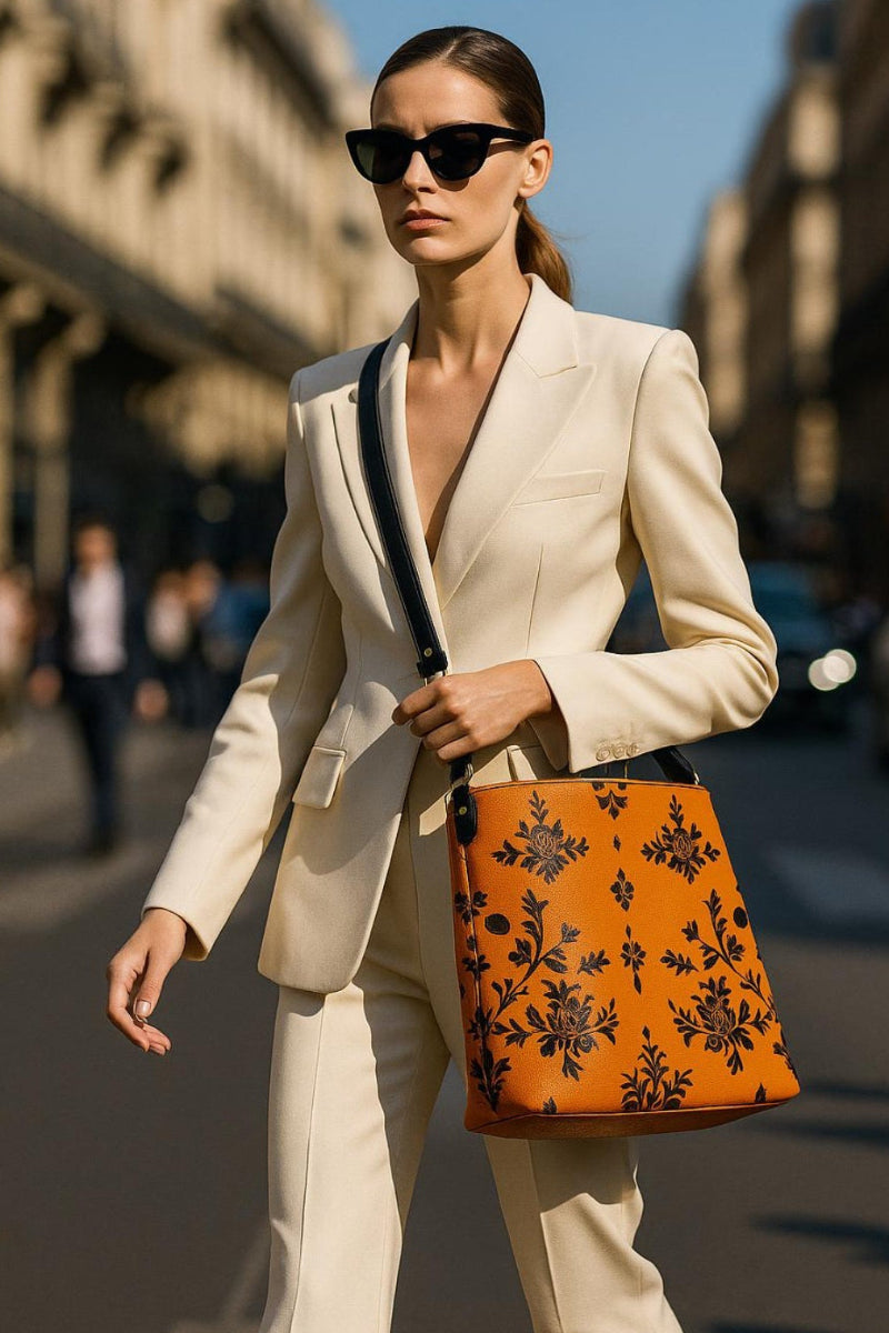 Woman wearing cream suit carrying orange baroque bucket bag with black floral print